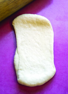 Overhead view of a piece of pretzel dough rolled out a bit to create a…